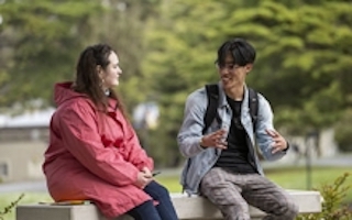 A woman and a man chat while sitting on benches on the SF State campus