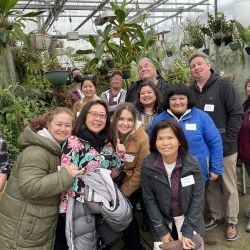 A group of people pse for a photo in a greenhouse with plants surrounding them
