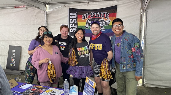 SF State staff huddle together inside of a booth decorate from SF State pride swag.